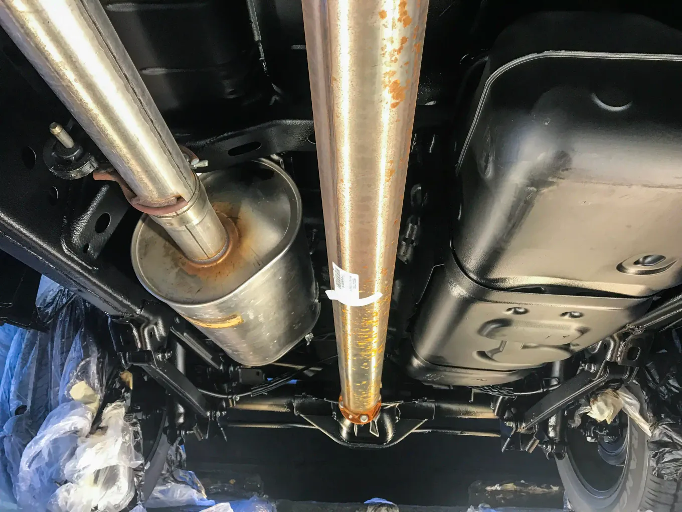 Truck undercarriage with fresh black rustproofing undercoating around the exhaust and fuel tank